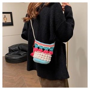 Close-up of handmade cherry knit bucket bag with elegant pearl chain shoulder strap