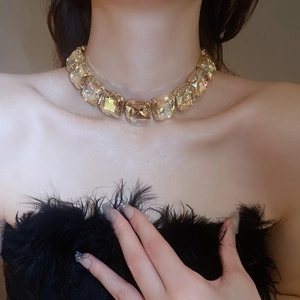 Close-up of luxury gold necklace with large square crystal worn with black feathers
