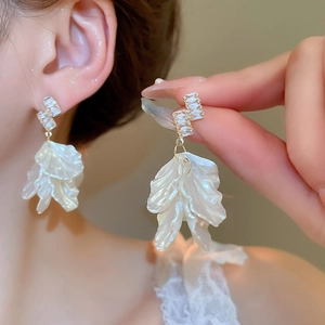 Macro view of gold zircon studs with elegant white ruffled shell flower petal tassels