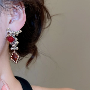 Close-up of asymmetric silver bow earrings with red resin pendant worn by a model