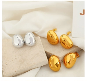 Polished egg-shaped metallic stud earrings in gold and silver finish on silk