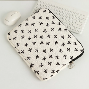Detail of quilted laptop sleeve with bow print, dual metal zippers on white desk