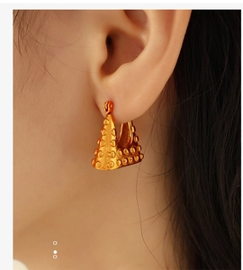 Close-up of golden triangular earrings with rivet texture on a female model