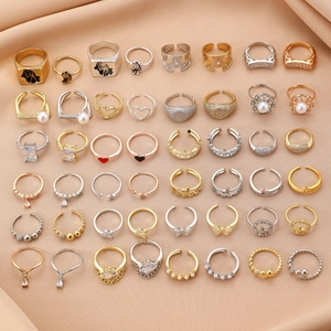 Flat lay of diverse gold and silver rings with pearls and zircon on beige silk fabric