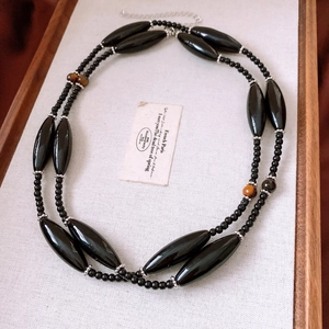 Detail of beaded necklace with tiger eye stones and black beads on linen tray