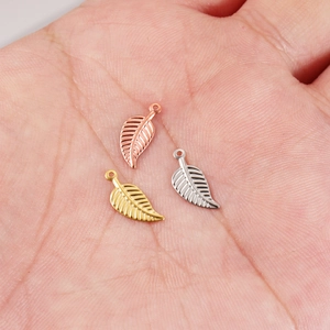 Polished stainless steel leaf charms in gold, silver, and rose gold on a palm
