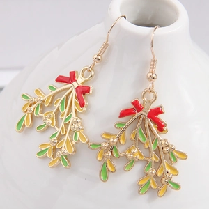 Elegant gold Christmas earrings with red bows and green leaves on a white ceramic stand