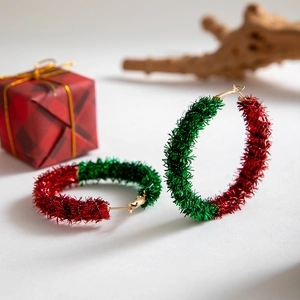 Close-up of red and green tinsel wreath hoop earrings next to a small festive gift box