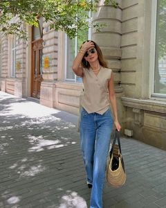 Detail of khaki asymmetrical sleeveless vest paired with blue jeans and straw handbag