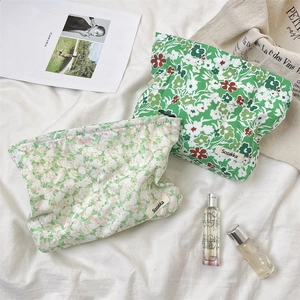 Flat lay of small green floral makeup bags on white linen with perfume and magazine