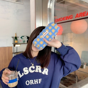 Blue and yellow checkered plush pencil case held by person in a cozy cafe setting