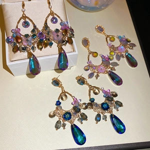 Macro detail of bohemian hollow gold earrings with colorful crystals and teardrop pendants