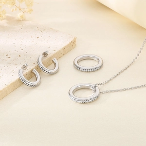 Detailed view of silver crystal C-shape necklace earrings and ring set on stone