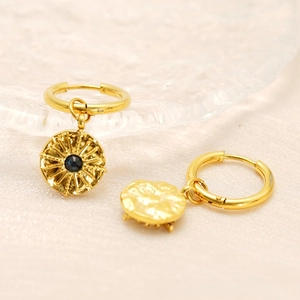 Detail of 18K gold earrings with sunburst pattern pendants and dark centered gemstones