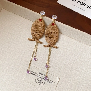 Detail view of woven rattan earrings with purple crystal teardrop tassels and gold chains