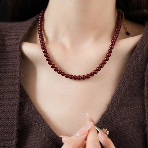 Macro detail of deep red round beaded necklace on model with polished finish