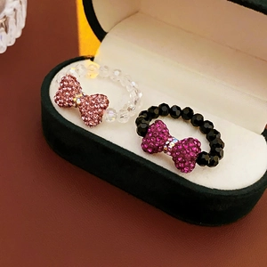 Macro detail of rhinestone bow beaded rings displayed in a green luxury jewelry box