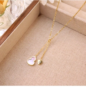 Detail of 18k gold plated titanium necklace with gourd and heart pendants on linen fabric