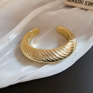 Détail du bracelet doré ovale avec texture en spirale et finition polie sur tissu de soie