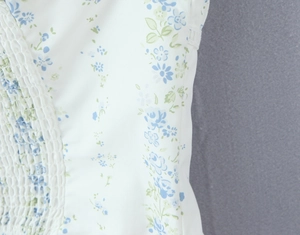 Detailed close-up of white floral fabric featuring smocking and light blue flower pattern