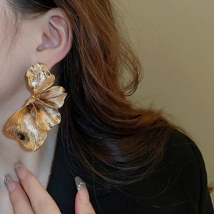 Detail of large golden petal earrings on model showing premium metallic texture