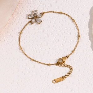 Detailansicht der 18K vergoldeten Kette mit Zirkonia-Blume und Perlen auf nassem Untergrund