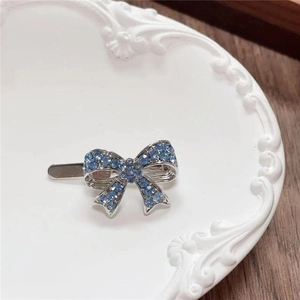 Close-up of a silver Y2K bow hair clip with blue rhinestones on a decorative plate