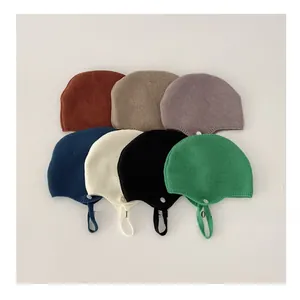 Flat lay of soft knitted baby earflap hats in seven assorted colors with chin straps