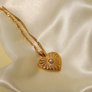 Détail du pendentif cœur doré avec texture ondulée et cristal sur tissu en soie