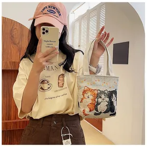 Detail of small beige canvas handbag featuring three cute cat illustrations and top handles