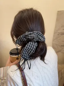 Detail of a black and white plaid scrunchie with a ribbon bow on a low ponytail hair