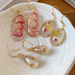 Detalle de pendientes de resina hechos a mano con flores secas reales en plato blanco