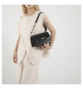 Détail d'un sac bandoulière vintage en cuir noir avec chaîne dorée porté par un mannequin