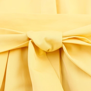 Detailed close-up of a decorative bow knot on the bright yellow woven fabric dress
