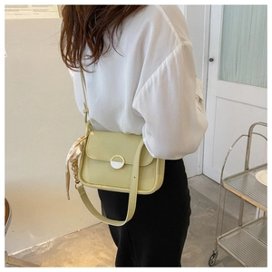 Detail of light green leather shoulder bag with metal buckle and printed silk scarf charm