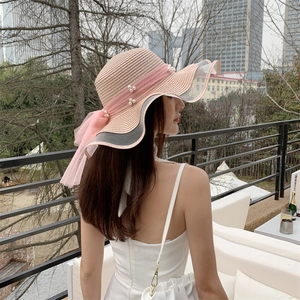 Detail of pink straw sun hat featuring a mesh bow, white pearls, and wavy brim for women