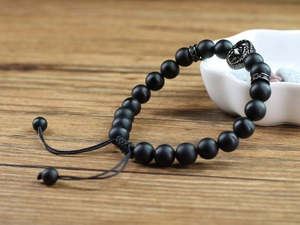 Macro shot of 8mm matte black beads and lion head charm on wooden tabletop with ceramic bowl
