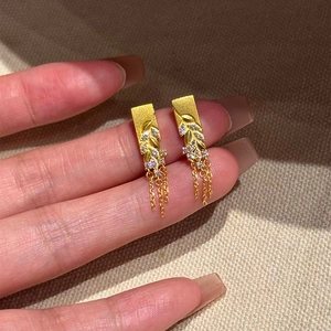 Boucles d'oreilles feuilles dorées avec texture mate et zircons tenues à la main
