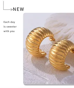 Macro view of wide C-shaped gold hoop earrings with polished vertical striped texture