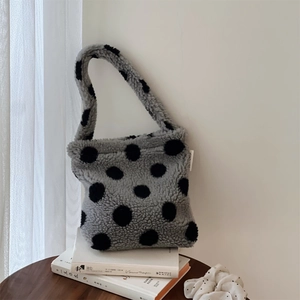 Sac à main chic en laine d'agneau grise à pois noirs posé sur une table en bois