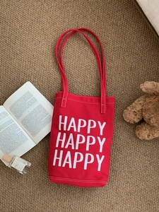 Detail of red canvas tote bag with white HAPPY lettering on a plush brown rug