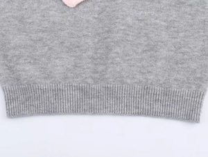 Detail of grey knitted sweater showing fine texture, ribbed hem and pink trim accents