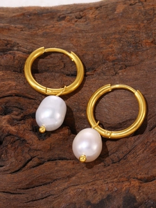 Macro view of gold-plated hoop earrings featuring elegant white teardrop pearls on wood