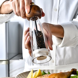 Manual acacia wood pepper grinder with clear acrylic body shown in a kitchen setting