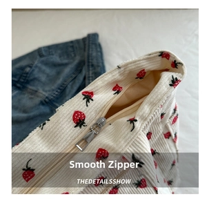 Close-up of smooth metal zipper closure on white corduroy tote bag with strawberry print