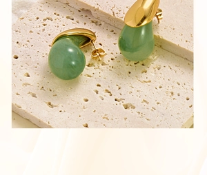 Close-up of teardrop-shaped gold earrings with transparent green resin on stone surface
