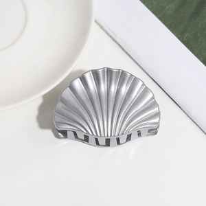 Detailed close-up of a silver metal shell hair claw clip on a minimalist white surface