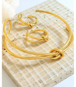 Close-up of golden dual-line knot bangle and rings set on a textured stone surface