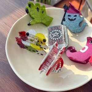 Macro shot of Halloween acrylic hair clips including spell book and ghost inside a ceramic bowl