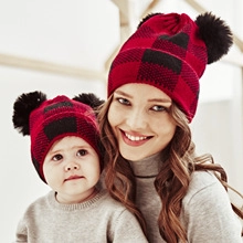 Close-up of mother and baby wearing matching red plaid knit beanies with black pom-poms